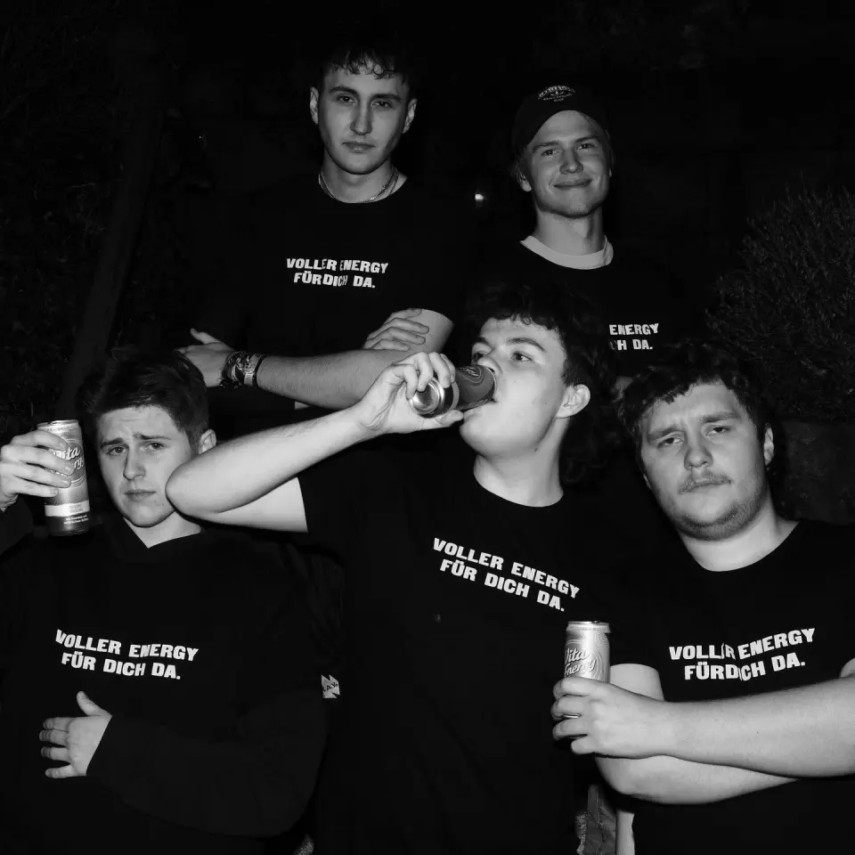 Fünf Freunde in schwarzen Shirts, einer trinkt gerade